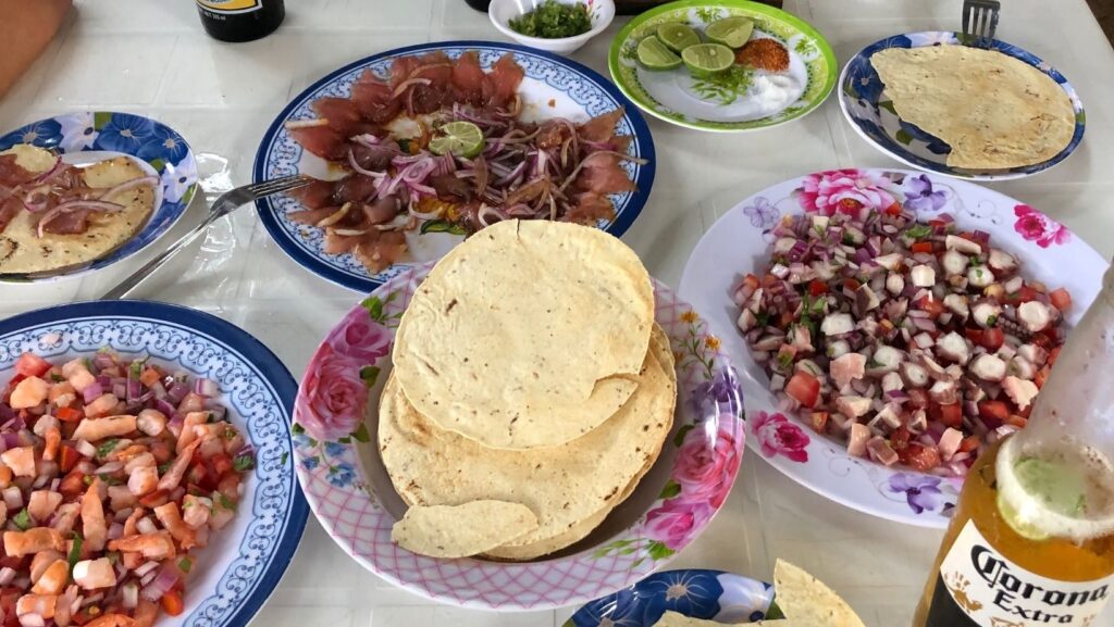 table with two plates of sashimi, tortillas, corona beers