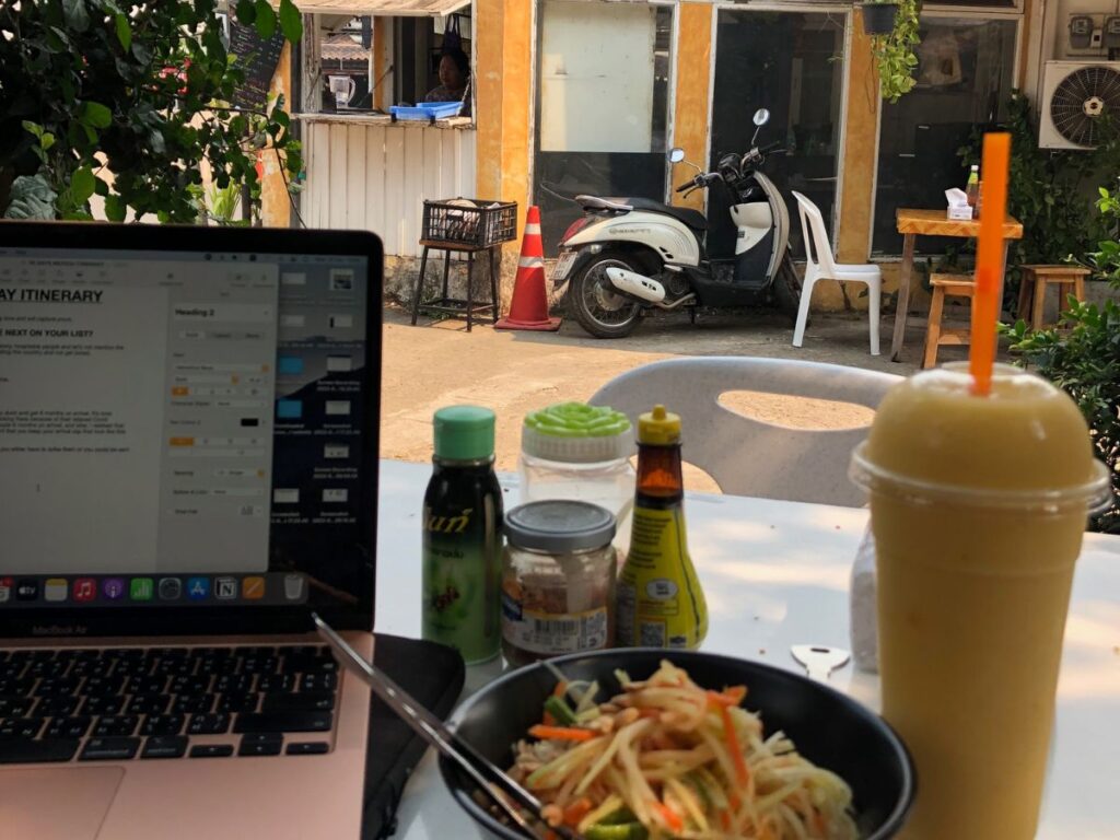 smoothie and papaya salad on table next to laptop, with joy's place, Pai in the background