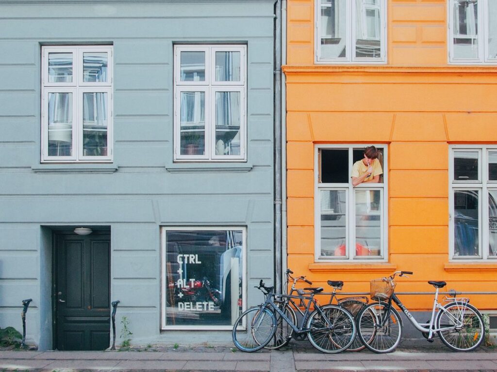 man looking out his window in a yellow house on a quiet street in Copenhagen