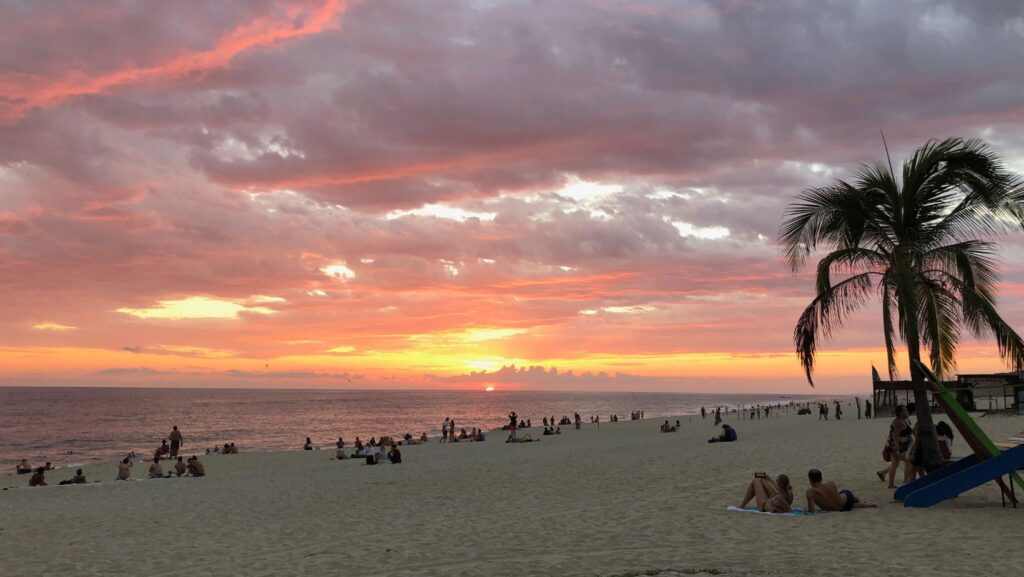 sunset at playa bacocho in puerto escondido with palm tree and lots of people watching sunset on sand