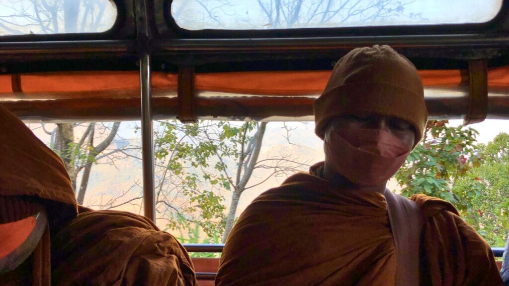 up close photo of monk in orange rope on the back of a Songthaew truck, Northern Thailand