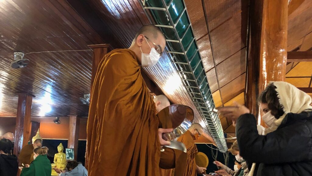 a girl on her knees offering rice to the monk at Wat Pa Tam Forest Monastery, Thailand