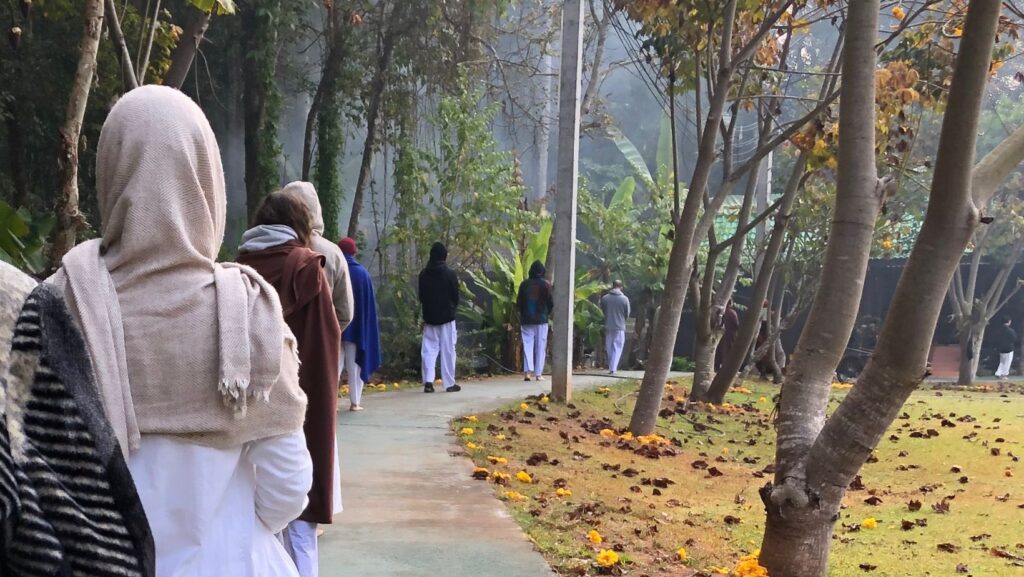 group of people walking in a line along a forest trail with eyes closed and head bowed