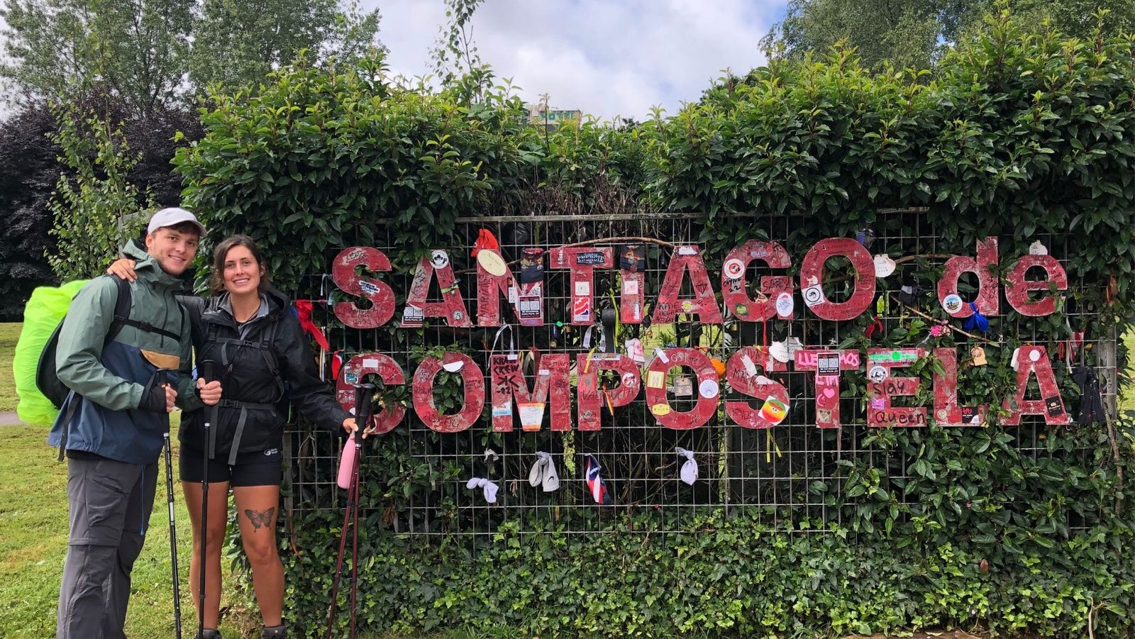 Two pilgrims in front of Santiago de Compestela sign after finishing the Camino de Frances route.